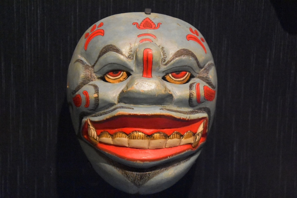  A blue and red colored traditional Indonesian mask with a smiling expression.